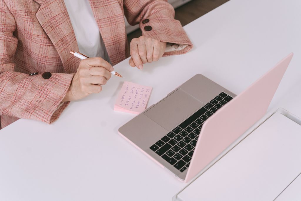 Businesswoman in a plaid jacket using a laptop and sticky notes for work planning.