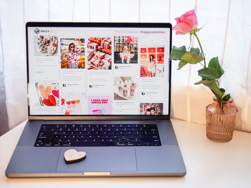 Laptop displaying Valentine's posts with a pink rose in a vase nearby, creating a romantic mood.